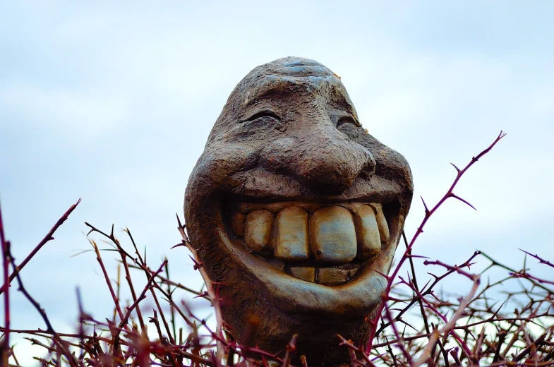 a statue of a man's face sticking out of a bush, by Aleksander Gierymski, trending on pixabay, big teeth smiling monster, portrait of a slightly rusty, laughing emoji, grinning lasciviously