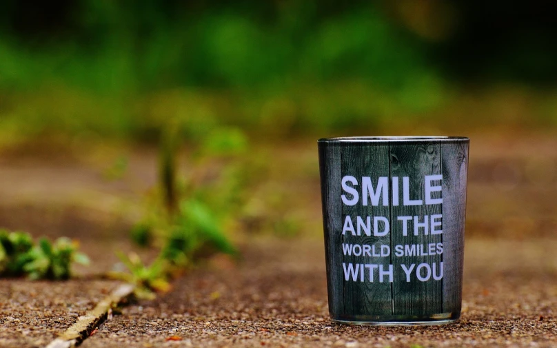 a can sitting on the ground with the words smile and the world smiles with you, a picture, by Mirko Rački, pexels contest winner, the sacred cup of understading, large black smile, a wooden, beutiful