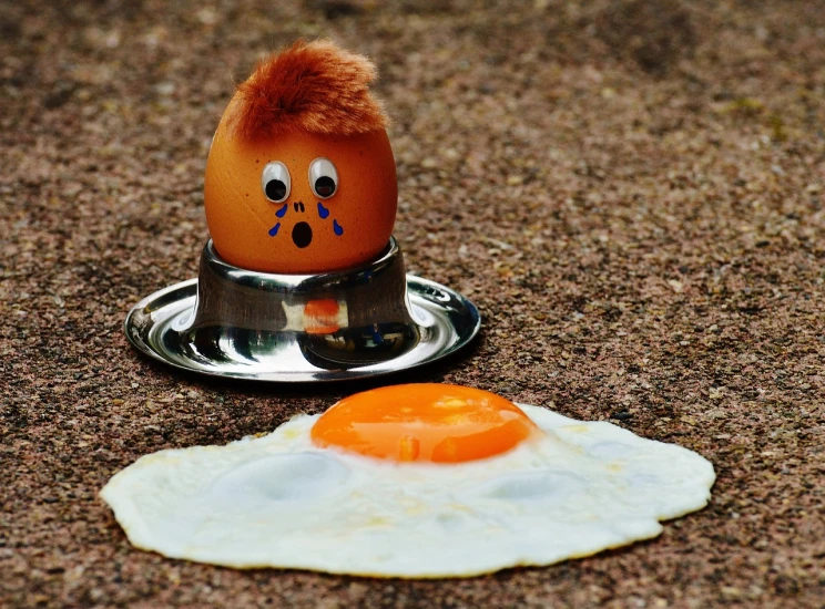 an egg sitting on top of a plate next to a fried egg, a photo, inspired by Károly Patkó, trending on pixabay, orange head, vin diesel head in egg cup, outside, worried