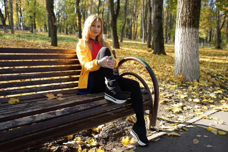 a woman sitting on top of a wooden bench, a portrait, by Maksimilijan Vanka, shutterstock, black and yellow tracksuit, autumn, sneaker photo, beautiful blonde girl