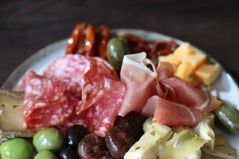 a close up of a plate of food on a table, mingei, cheese and salami on the table, olives, pork, glazed