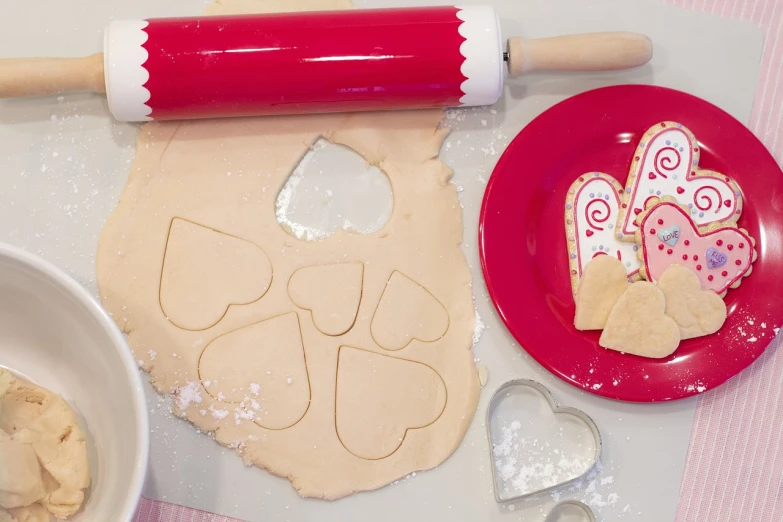 a red plate topped with cookies next to a rolling pin, by Sylvia Wishart, forming a heart with their necks, candy decorations, closeup photo, high res photo