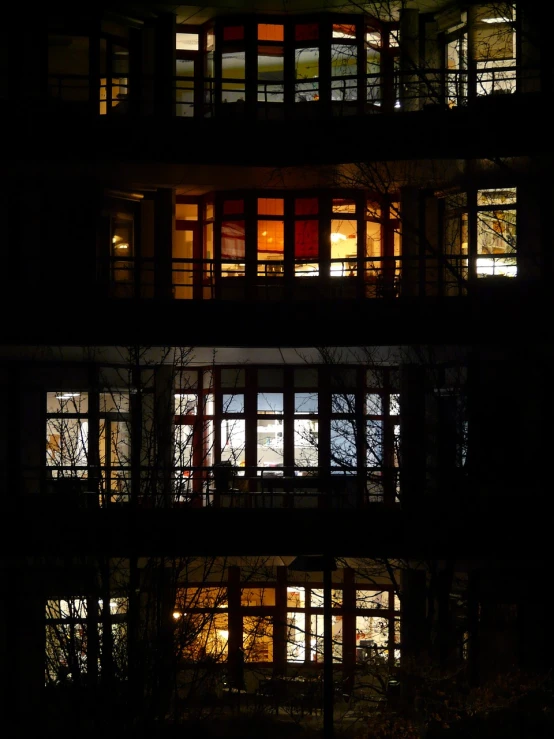 a tall building with lots of windows lit up at night, inspired by André Kertész, flickr, difraction from back light, pleasant cozy atmosphere, winter night, with backlight
