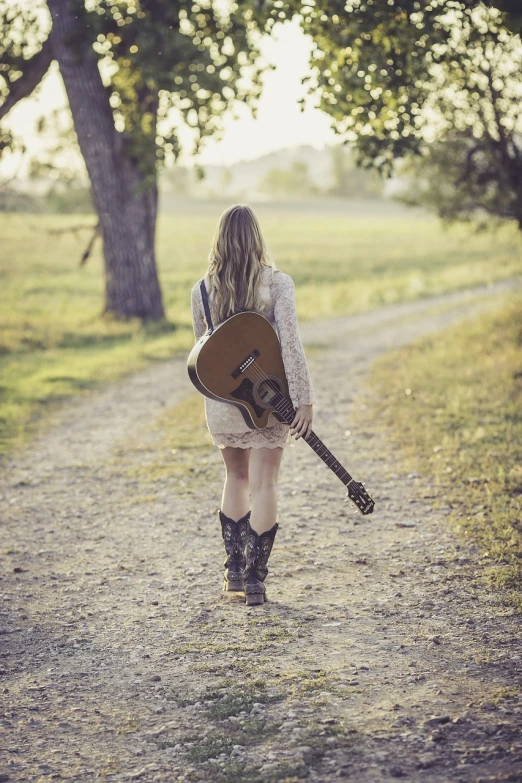 a woman walking down a dirt road holding a guitar, a picture, shutterstock, trending photo, blonde girl, old color photo, ox