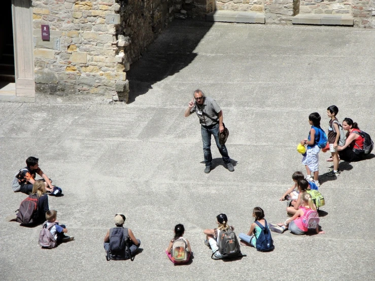 a man standing in the middle of a circle of people, a photo, figuration libre, carcassonne, children drawing, stand on stone floor, on a sunny day