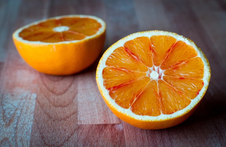 an orange cut in half on a wooden table, by Etienne Delessert, pexels, stock photo, image split in half, half red, juicy color