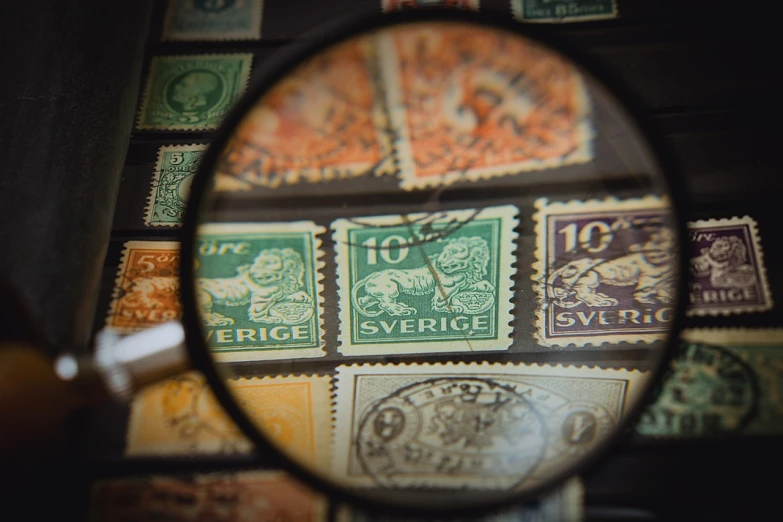 a magnifying glass over a collection of stamps, by Jesper Knudsen, pexels contest winner, symbolism, sweden, 1900s photo, 🦩🪐🐞👩🏻🦳, !!! shallow depth of field!!!
