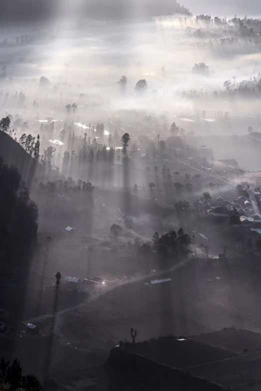 the sun shines through the clouds over a village, a picture, by Daren Bader, sumatraism, foggy volumetric light morning, helicopter view, small streaks of light through, gray fog