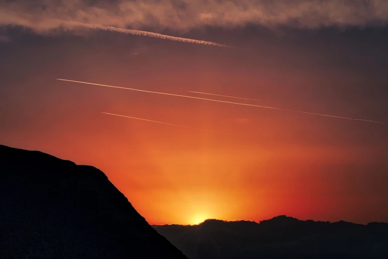 a plane flying over a mountain at sunset, by Hans Schwarz, streaks, suns, closeup photo, trinity