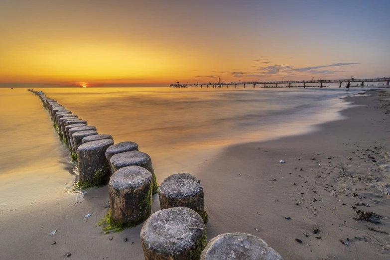 a row of wooden posts sitting on top of a sandy beach, a picture, by Holger Roed, shutterstock, 8k hdr sunset lit, fallen columns, stock photo, long exposure photo