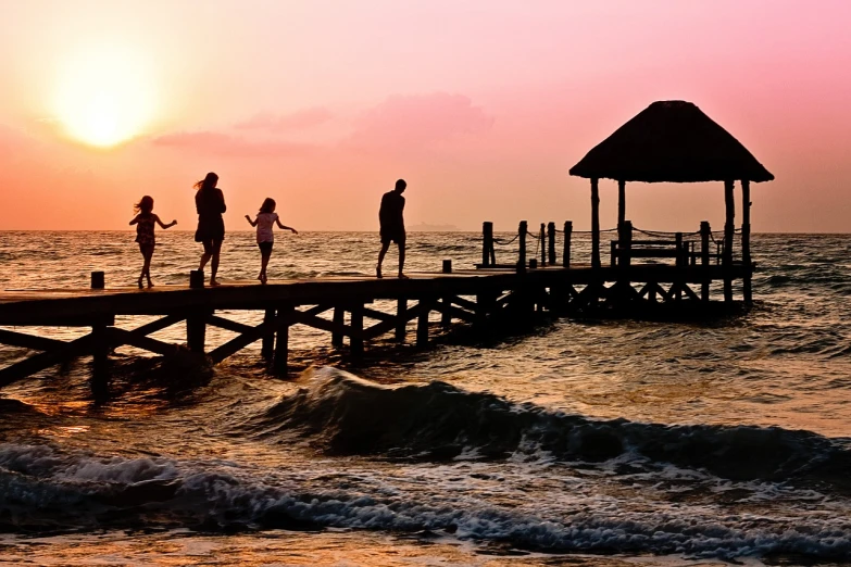 a group of people standing on a pier at sunset, a picture, by Brad Holland, shutterstock, families playing, paradise, carefree, siluette