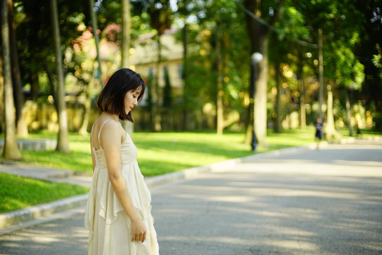 a woman standing in the middle of a road, a picture, inspired by Kim Du-ryang, shutterstock, sunny day in a park, maternity feeling, sorrow, wearing ivory colour dress