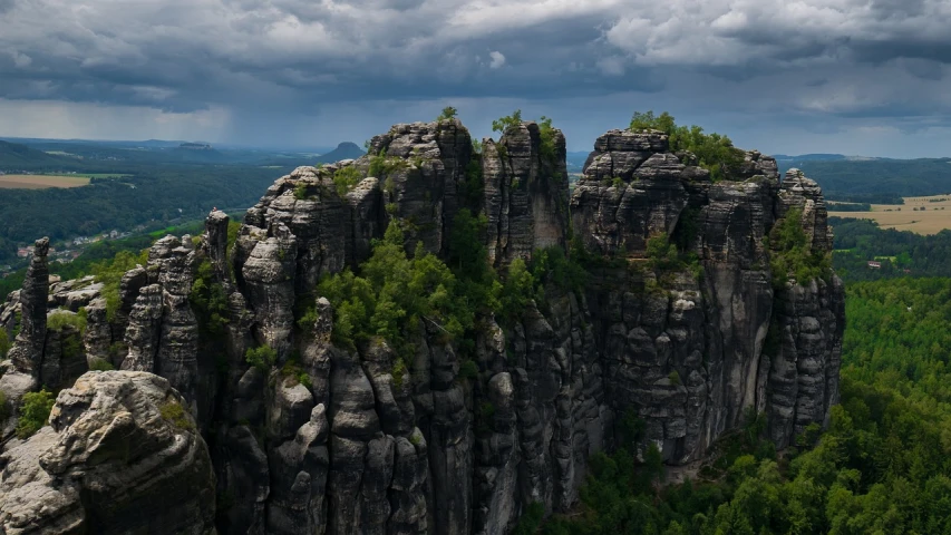 a group of rocks sitting on top of a lush green hillside, a detailed matte painting, pexels contest winner, german romanticism, germany. wide shot, rocky cliff, on a cloudy day, 4k drone photography