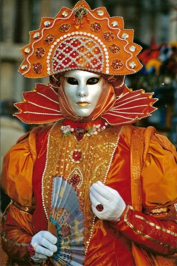 a close up of a person wearing a mask and holding a fan, inspired by Quirizio di Giovanni da Murano, flickr, (tom cruise!!!!!) jester costume, orange halo around her head, gorgeous and huge head ornaments, fujicolor sample