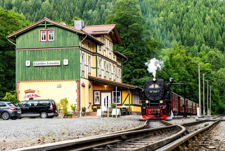 a train traveling down train tracks next to a building, shutterstock, heidelberg school, hideen village in the forest, !!beautiful!!, 🚿🗝📝, trains in the background