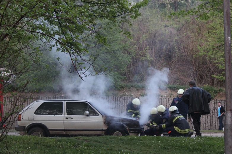 a group of people standing around a car with smoke coming out of it, a photo, by Jan Konůpek, shutterstock, fireman sam, crashed in the ground, ae 8 6, news photo