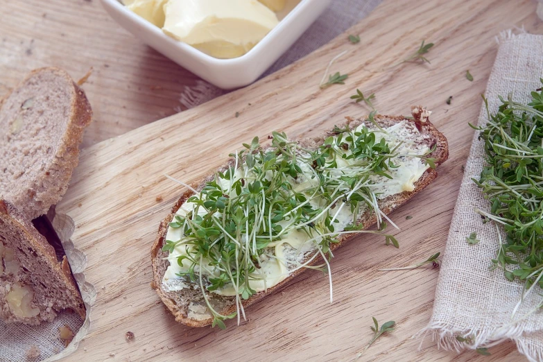 a piece of bread sitting on top of a wooden cutting board, pexels, art nouveau, herbs, salad and white colors in scheme, high res photo, butter