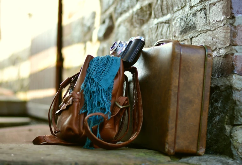 a piece of luggage sitting next to a brick wall, a picture, by Christen Dalsgaard, pixabay, happening, holster, brown and cyan color scheme, soft warm light, lacey accessories