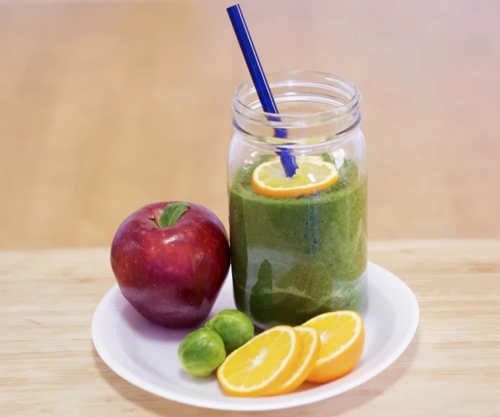 a green smoothie sits on a plate next to an apple, bright green dark orange, full scene shot, 💣 💥, high res