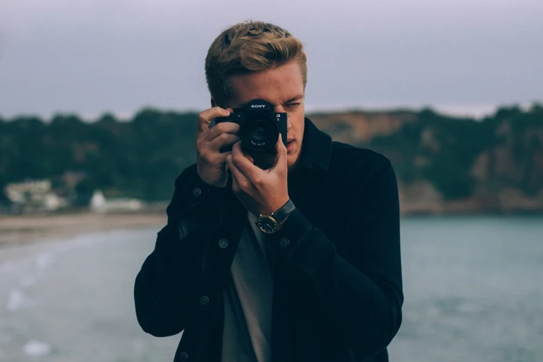 a man taking a picture with a camera, a picture, by Austin English, unsplash, realism, blonde british man, young man with short, greg rutkowski uhd 8k, on the coast