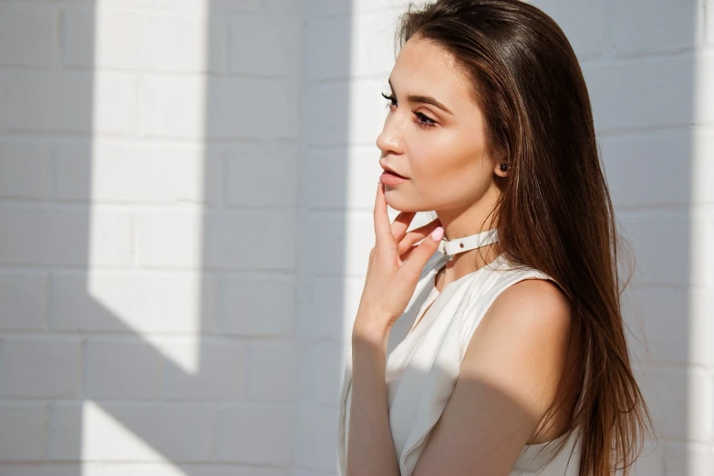 a woman standing in front of a white brick wall, by Emma Andijewska, shutterstock, romanticism, on a young beautiful woman neck, soft shadow, wearing collar, perfect crisp sunlight