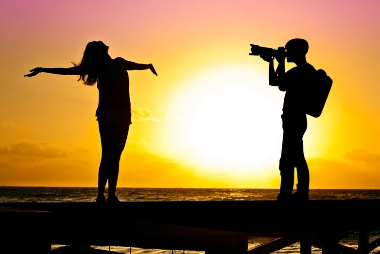 a couple of people standing on top of a pier, a picture, art photography, paparazzi photo, sunset photo, pointing at the camera, shot with a canon