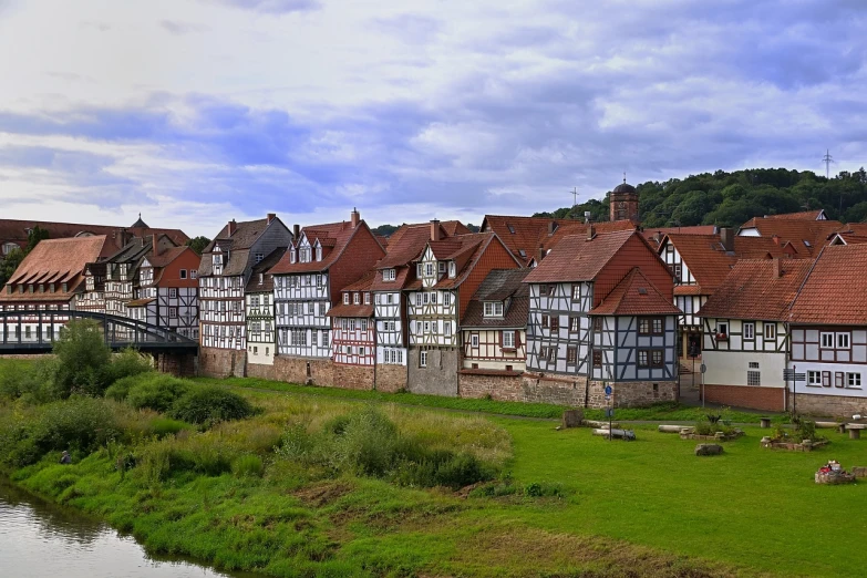 a group of buildings sitting next to a river, a photo, by Juergen von Huendeberg, renaissance, lower saxony, wooden structures, hills, elegant look