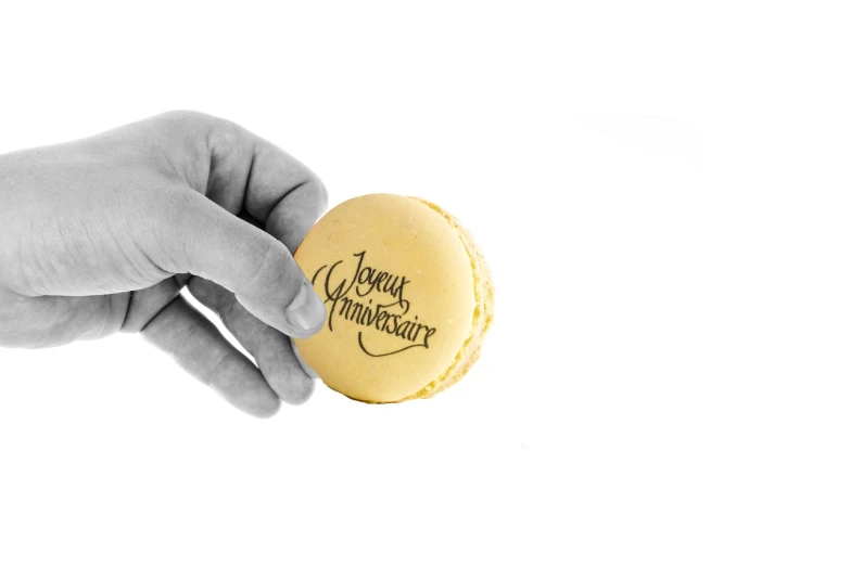 a black and white photo of a hand holding a macaron, inspired by Avgust Černigoj, art nouveau, he is! about 3 0 years old, yellow, high resolution product photo, logo