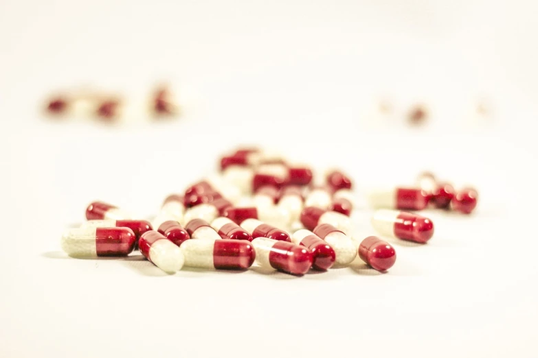 a pile of red and white pills on a white surface, a tilt shift photo, antipodeans, crimson and ecru color scheme, 4 k product photo, very sharp photo