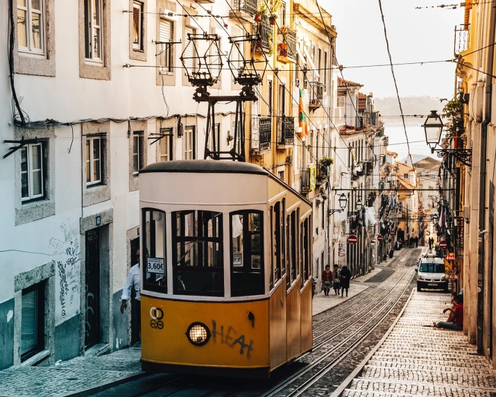 a yellow trolley traveling down a street next to tall buildings, by Matija Jama, pexels contest winner, renaissance, lisbon, 🦩🪐🐞👩🏻🦳, warm light, chairlifts