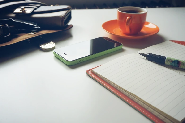 a cup of coffee and a cell phone on a table, sitting at desk, green and orange theme, professional iphone photo, high-res