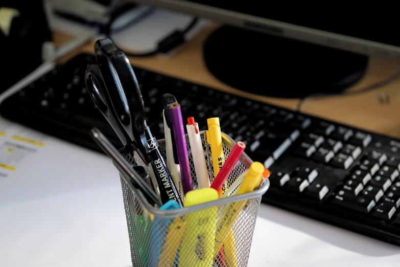 a cup filled with pens and markers next to a keyboard, by Randy Post, pexels, afp, ¯_(ツ)_/¯, office cubicles, 2 4 mm iso 8 0 0 color