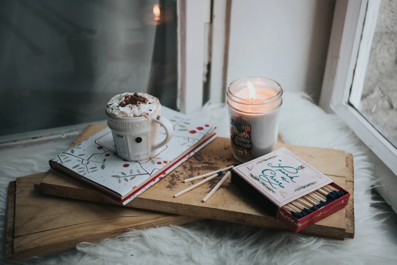 a cup of hot chocolate next to matchsticks and a candle, a picture, by Aleksander Gierymski, pexels, flatlay book collection, white candles, inside a cozy apartment, with a wooden stuff
