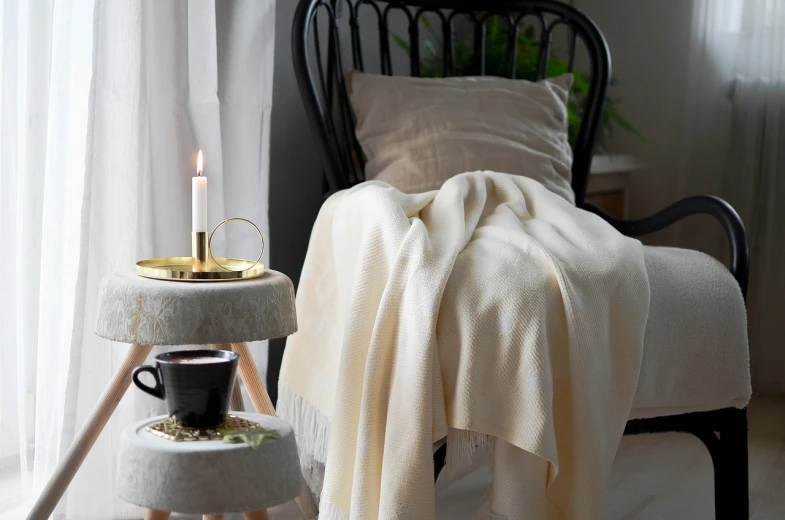 a white blanket sitting on top of a table next to a chair, inspired by Einar Hakonarson, holding a candle holder, productphoto, cozy home background, ecru cloth