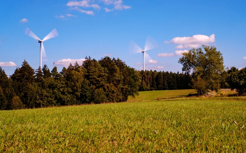 a group of wind turbines on top of a lush green field, a stock photo, by Thomas Häfner, next to farm fields and trees, ultrawide establishing shot, shot on nikon z9, interesting background