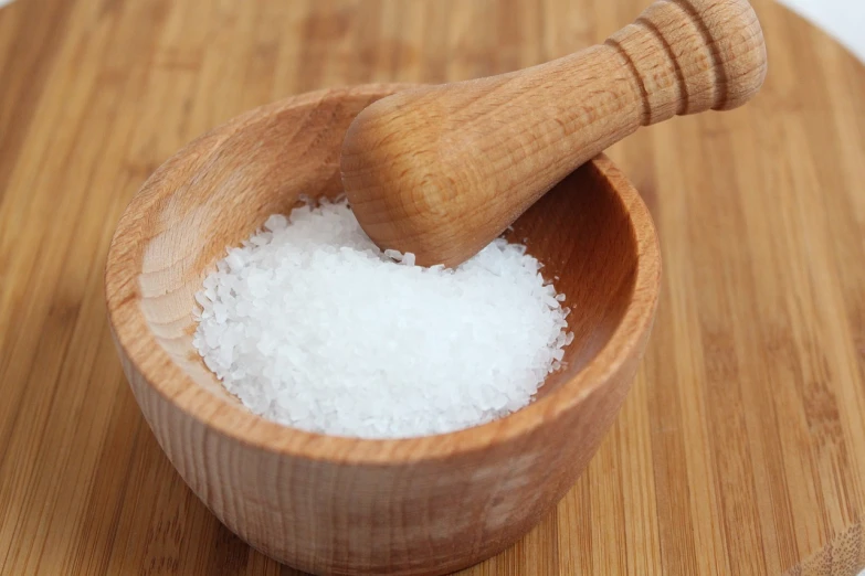 a wooden bowl filled with white salt on top of a wooden table, photograph credit: ap, shiny skin”, unwind!, smooth!]