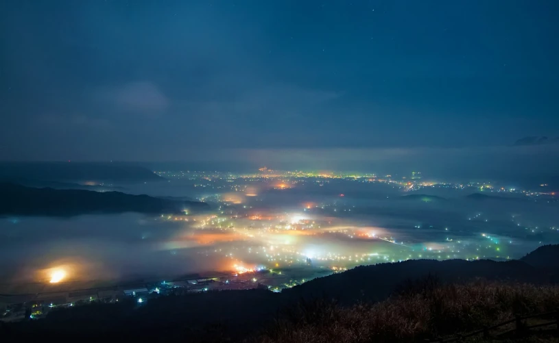 a view of a city at night from the top of a hill, pexels, mingei, foggy photo 8 k, ehime, tonemapping, distant town in valley and hills
