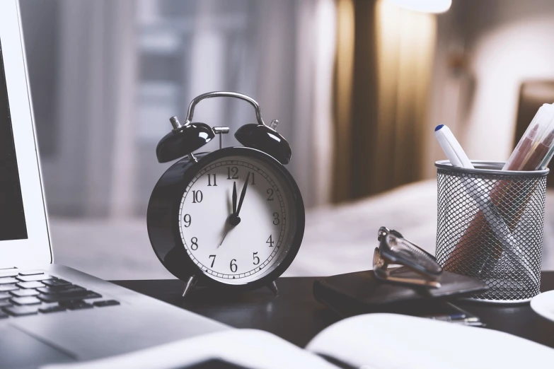 an alarm clock sitting on top of a desk next to a laptop, happening, timeless, photo taken in 2018, clocks, low light