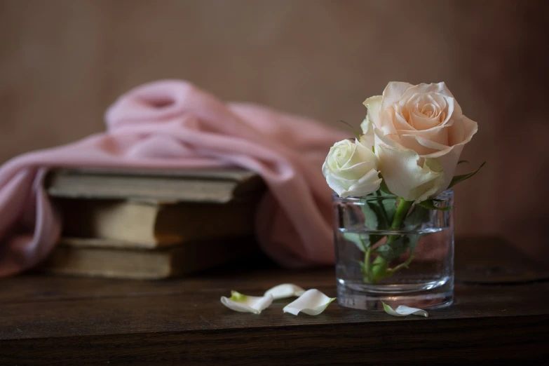 a vase filled with flowers sitting on top of a wooden table, a still life, shutterstock, romanticism, wooden desks with books, melanchonic rose soft light, close up portrait photo, white and pink cloth