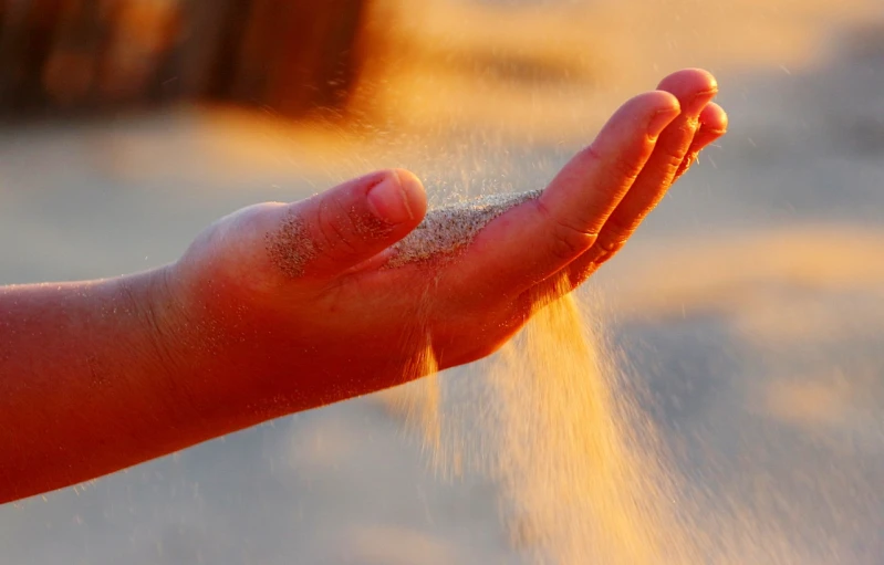 a person's hand is sprinkled with sand, by Julian Allen, radiant morning light, wallpaper mobile, precious moments, authoritative