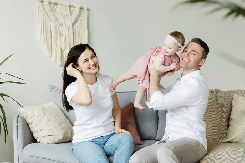 a man and woman sitting on a couch holding a baby, inspired by The Family Circus, shutterstock, white trendy clothes, happy girl, background image, on a couch