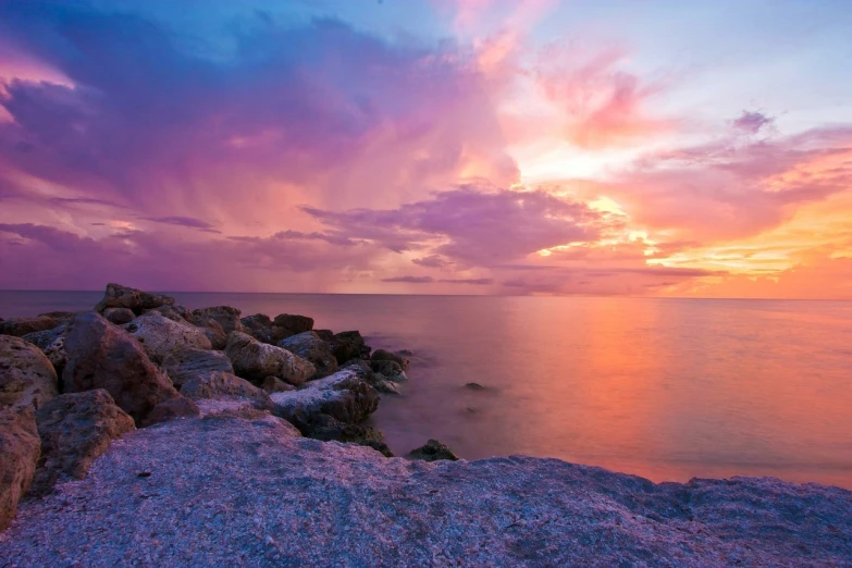 a sunset over the ocean with rocks in the foreground, a picture, pexels, romanticism, pink and purple, amazing sky, colorful hd picure, wideshot