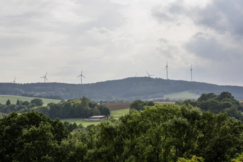 a group of wind turbines sitting on top of a lush green hillside, by Karl Hagedorn, renaissance, wide view of a farm, german forest, far away from camera, urban surroundings