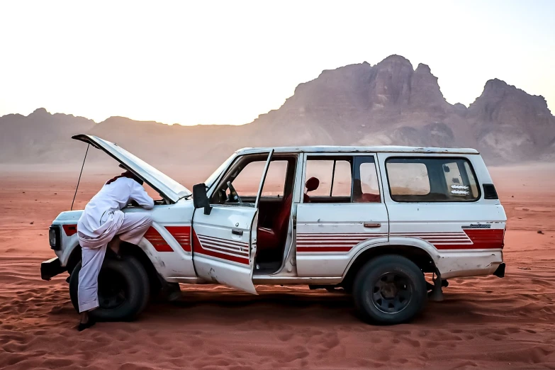 a man standing next to a car in the desert, by Ibram Lassaw, pexels contest winner, fine art, white red, everyone having fun, injured, panorama shot