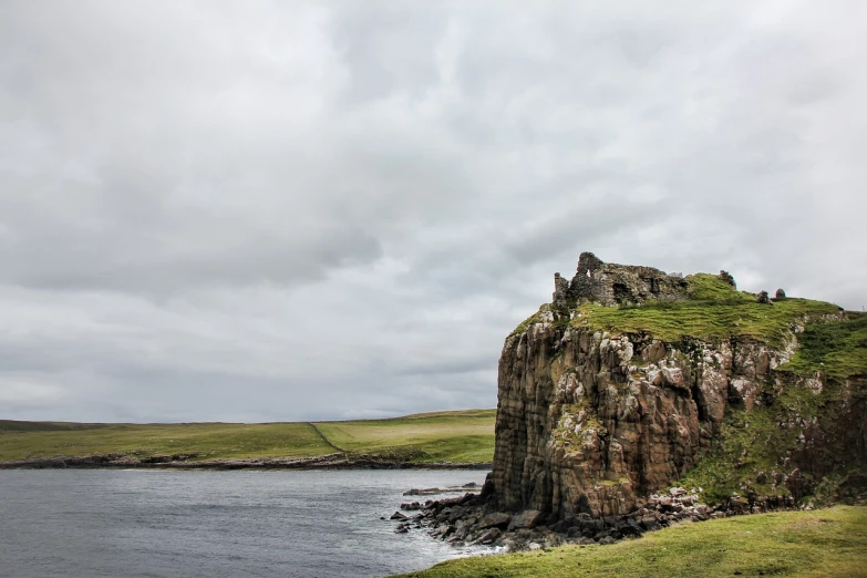 a group of sheep standing on top of a lush green hillside, a tilt shift photo, by John Murdoch, romanticism, the rock is in the sea, tall castle enclosed palisaded, orkney islands, location of a dark old house