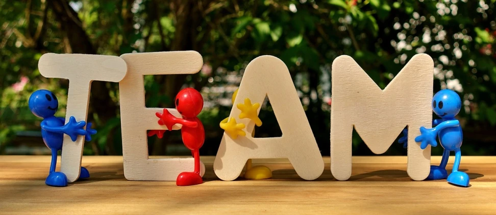 a group of small figurines standing next to the word team, by Fan Qi, pixabay contest winner, fine art, doing a sassy pose, a wooden, sunny morning, red writing