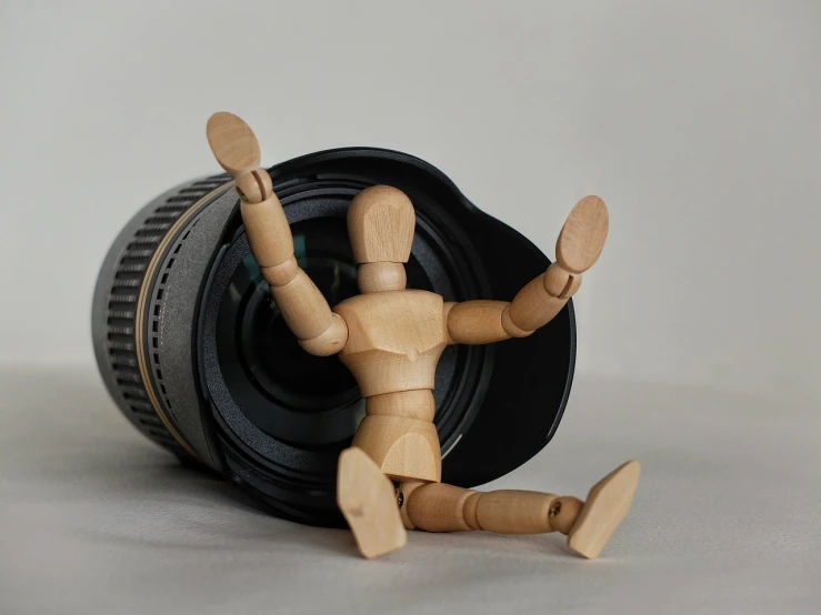 a wooden mannequin sitting next to a camera lens, a picture, photorealism, funny professional photo, desperate pose, toy photo, filling the frame