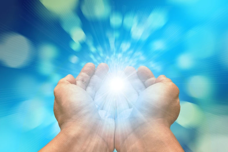 a person holding their hands in front of a bright light, a stock photo, light and space, healing energy, with a blue background, abundant detail, radiant halo