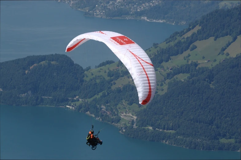 a person paragliding over a large body of water, a picture, by Bernard Meninsky, shutterstock, swiss, ornithopter, 2009, photos