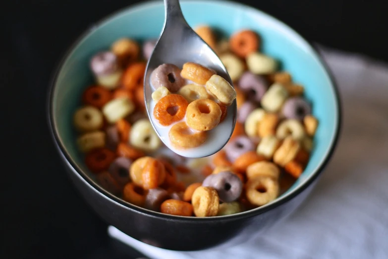 a spoon full of cereal sitting on top of a bowl, orange and turquoise ans purple, milk, petite, slight grain